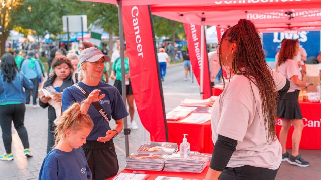 A woman and her child talk to a volunteer at an information booth