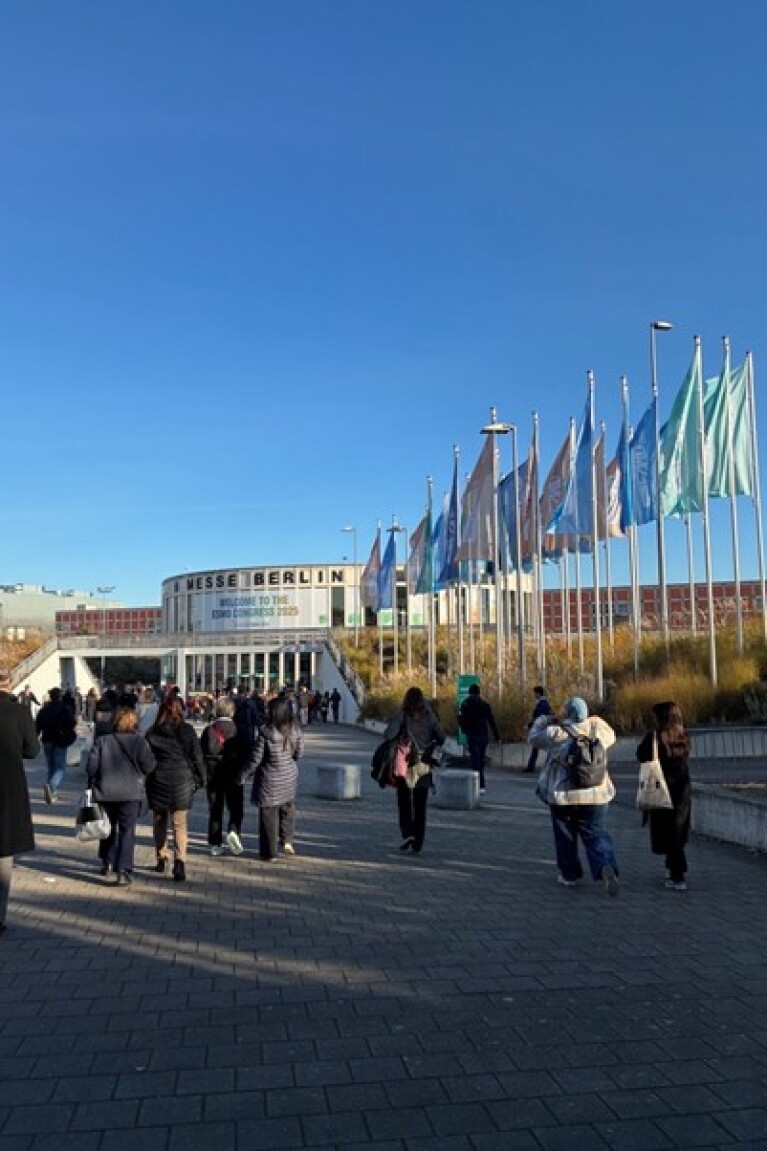 Auf dem Bild sind Menschen auf dem Weg zum Eingang der Messe Berlin zu sehen. Auf einem Banner steht: „Welcome to the ESMO congress 2025“.