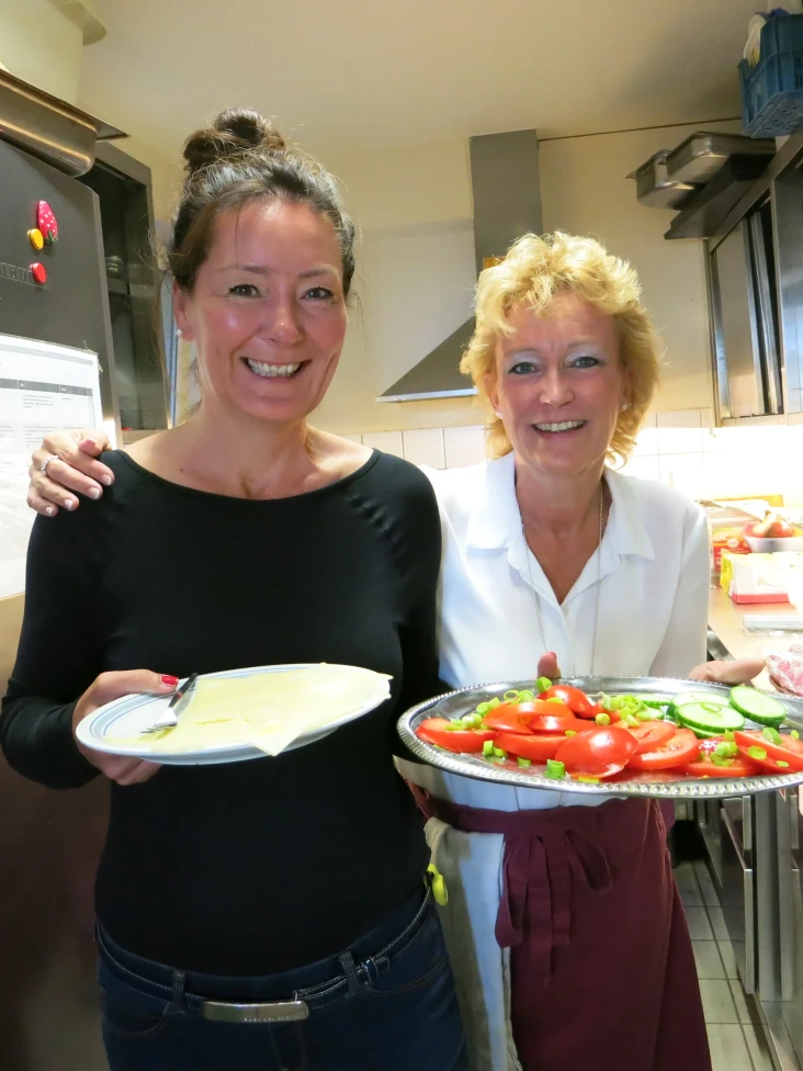 Zwei Mitarbeiterinnen von J&J in einer Großküche, die Teller mit Lebensmitteln tragen.