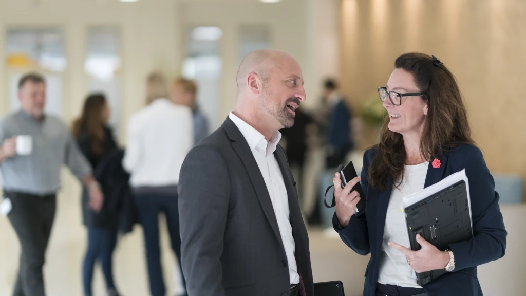 Zwei Mitarbeitende stehen im belebten Foyer und unterhalten sich.