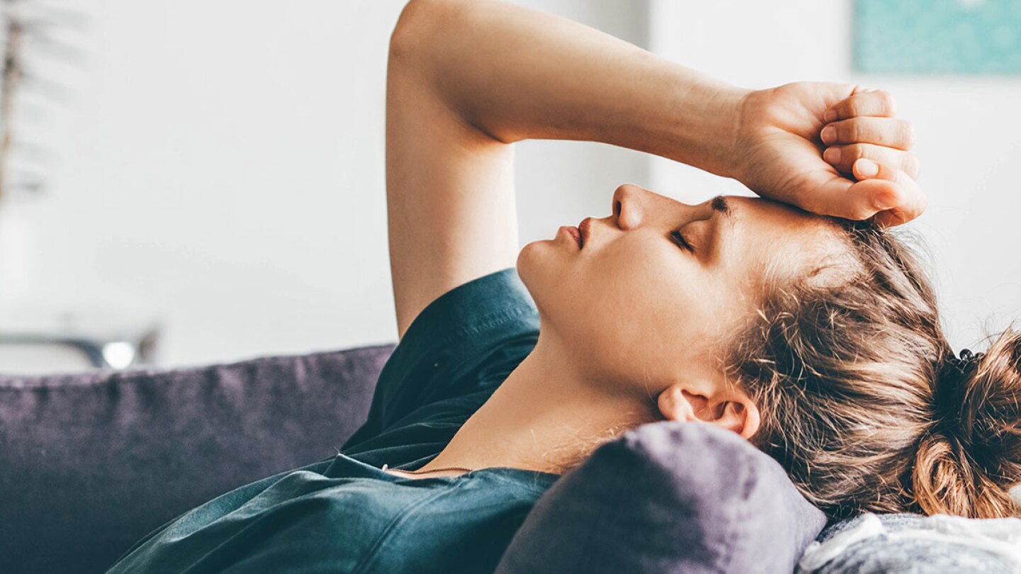 A stressed woman on the couch holding her hand to her head 