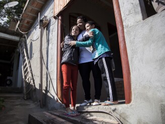 A woman and her children embrace in the doorway of their home.