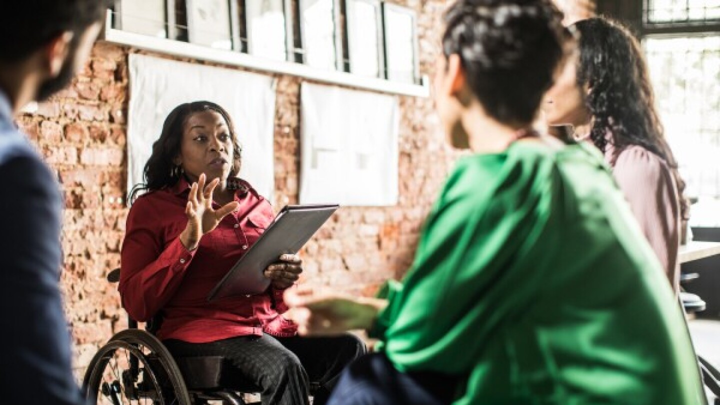 A woman in a wheelchair holding a clipboard and presenting during a meeting 