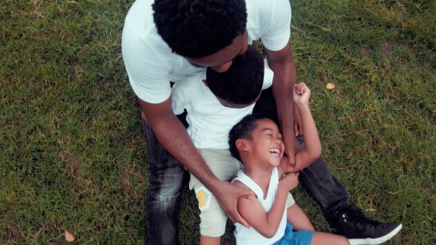 A father plays with this two kids on the grass