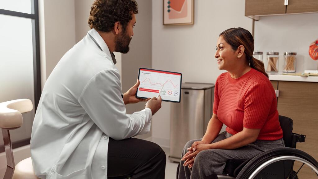 Profesional de la salud compartiendo información en un tablet a una mujer en silla de ruedas.