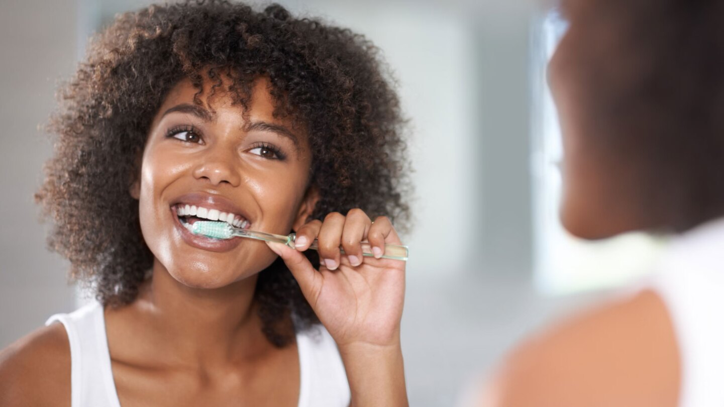 woman brushing her teeth in bathroom mirror