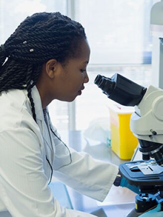 Black female scientist using microscope