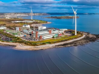 A photo of a production facility, including wind turbines, surrounded by water