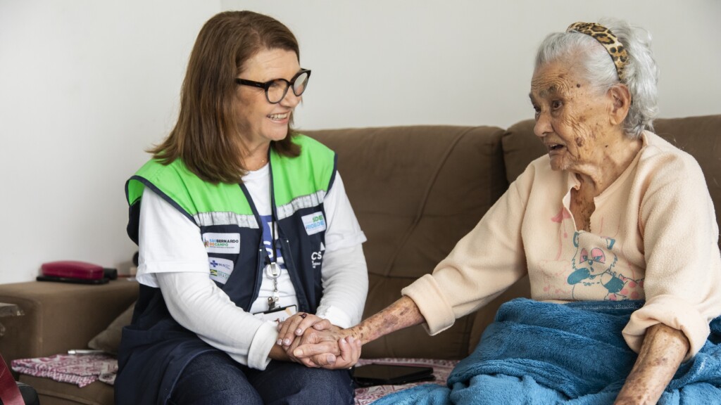 Healthcare worker holding hands with an elderly woman on a couch.