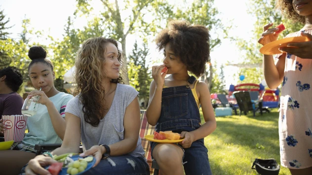 Mehrere Kinder und Frauen sitzen im Garten und essen Obst.
