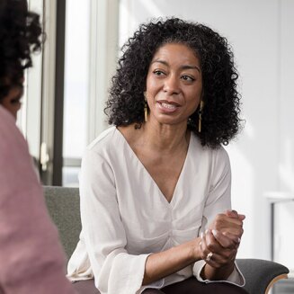 A woman clasping her hands speaking with a psychiatrist slightly out of frame