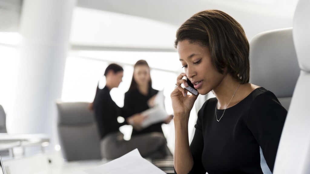 A black business woman speaking on a smartphone at her desk
