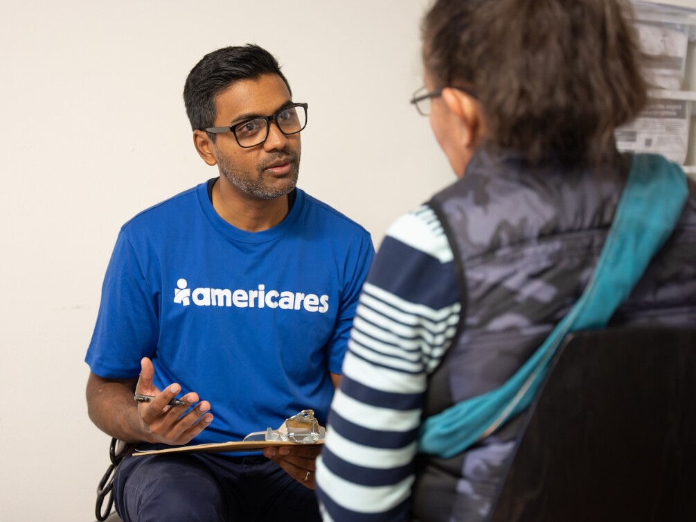 Americares volunteer in a blue shirt speaks with a community member during a disaster relief effort.