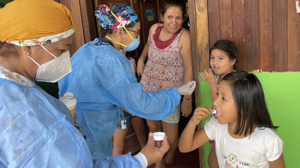 Two nurses in PPE delivering medicine to a family on their doorstep 