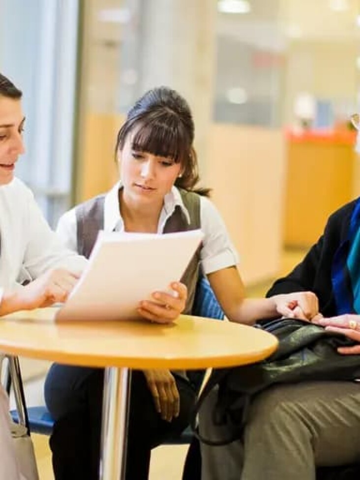 Eine Medizinerin spricht mit einer Patientin im Rollstuhl und einer Angehörigen