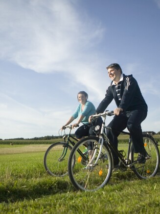 A smiling man and woman riding their bikes in a field