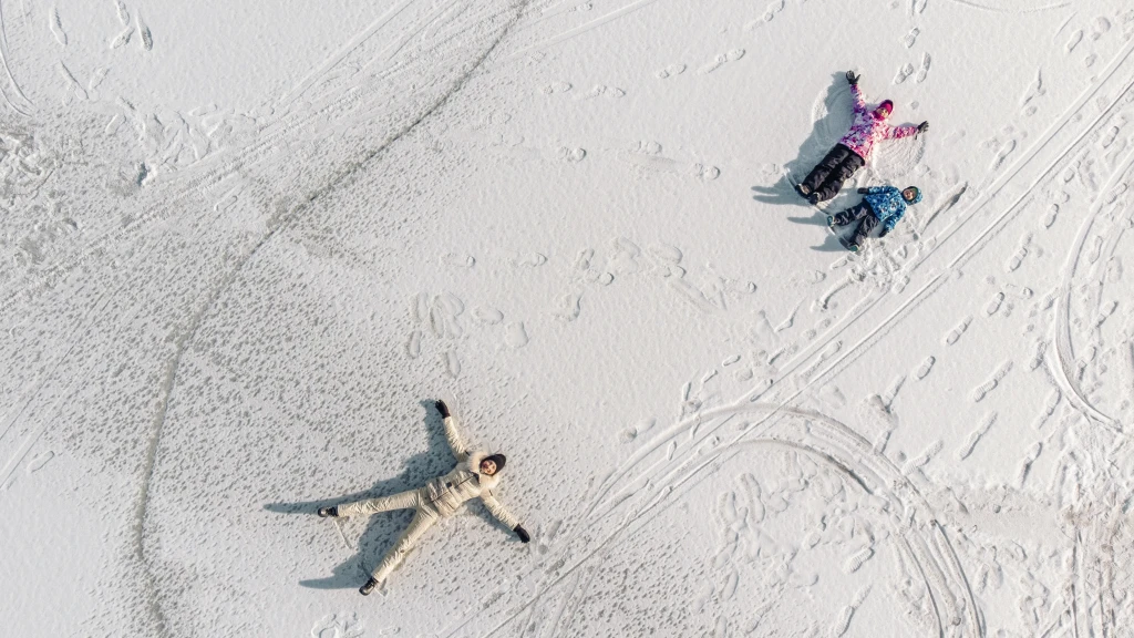 Luftaufnahme einer Familie, die Schneeengel macht.