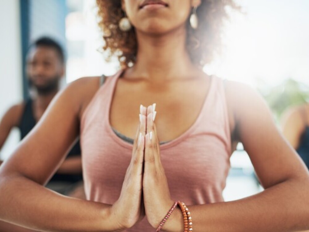 A close up of a woman practicing yoga with her hands clasped together at the center of her chest 